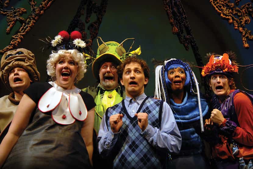 Six actors in vibrant costumes wear surprised expressions as they perform on stage at a...