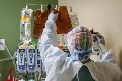 A health care worker changes out an intravenous drip while treating an intubated patient in...