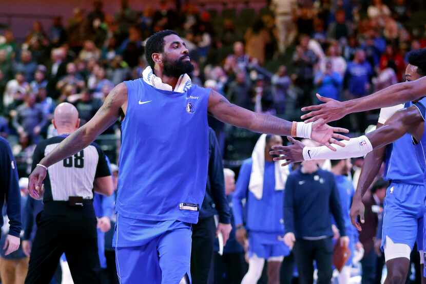 Dallas Mavericks guard Kyrie Irving slaps hands with teammates as he walks to the locker...