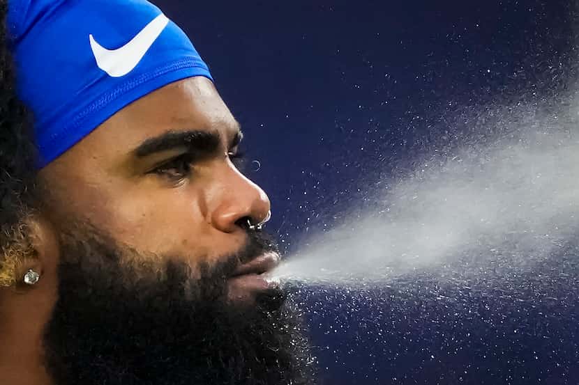 Dallas Cowboys running back Ezekiel Elliott blows water as the team warms up before an NFL...