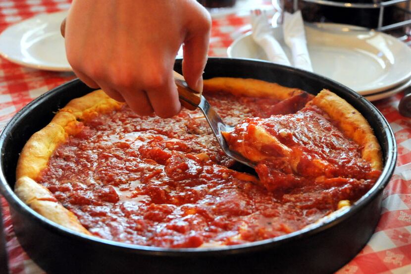 A server slices a piece of deep dish pepperoni pizza for a customer at Gino's East Chicago...
