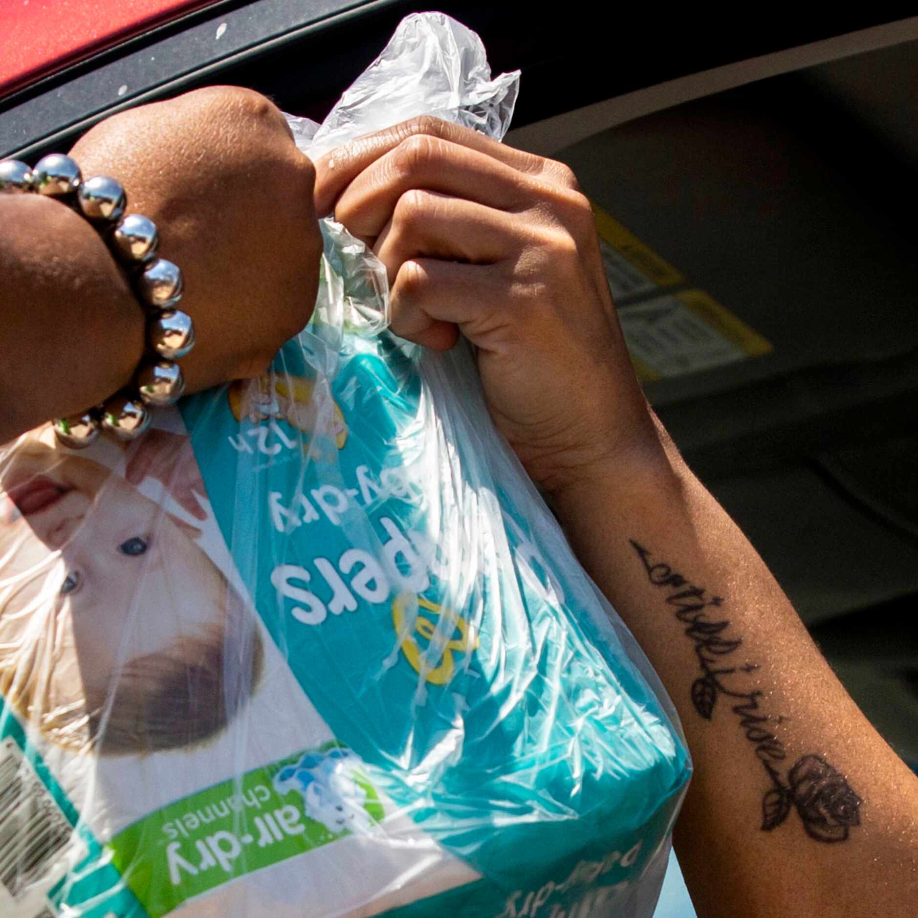 Executive Consultant Teirney Guinyard (left) hands diapers to a woman during a drive-through...