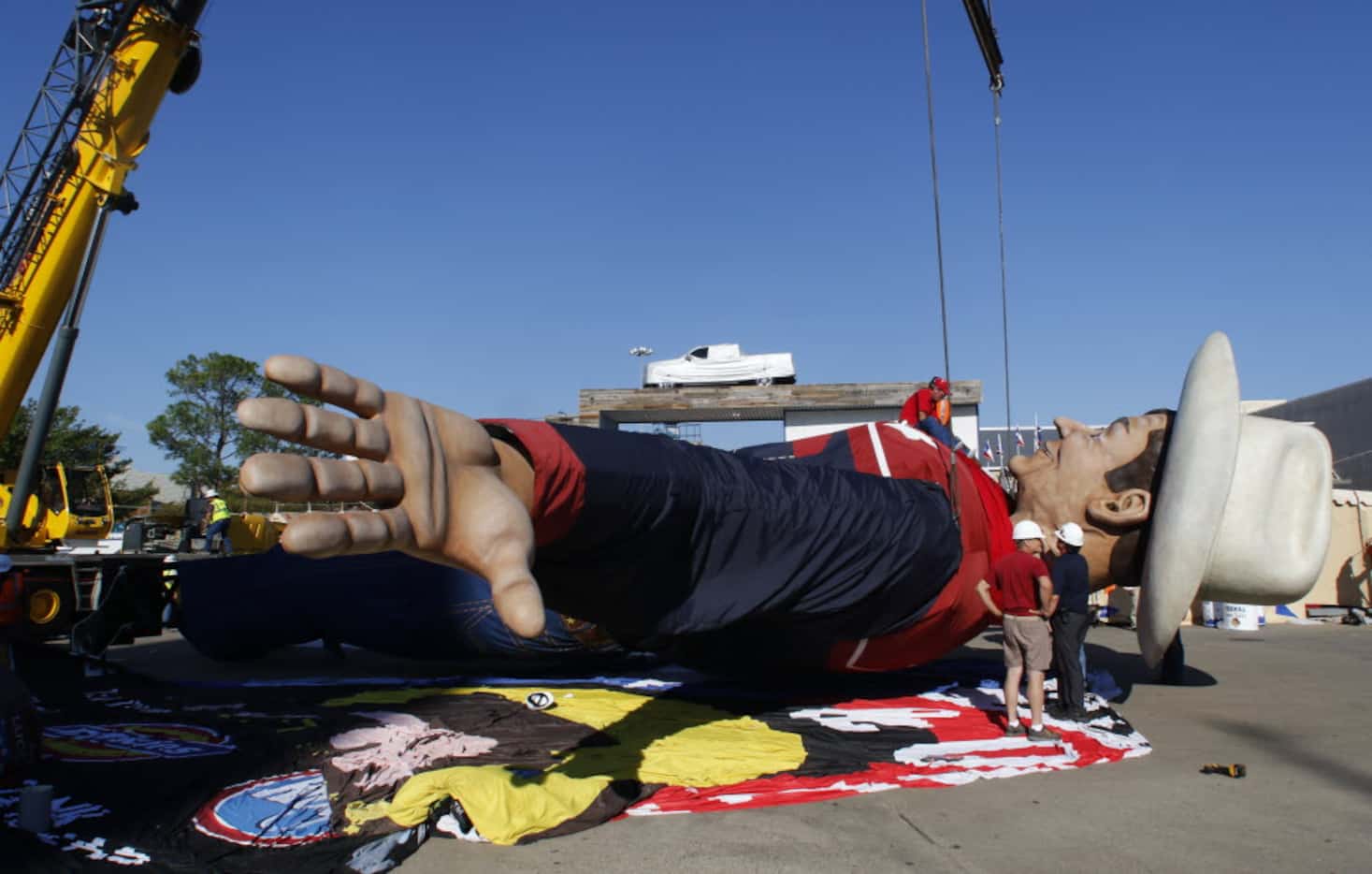 Workers sit on Big Tex’s chest as they adjust his western shirt that runs a size 200 x 325,...