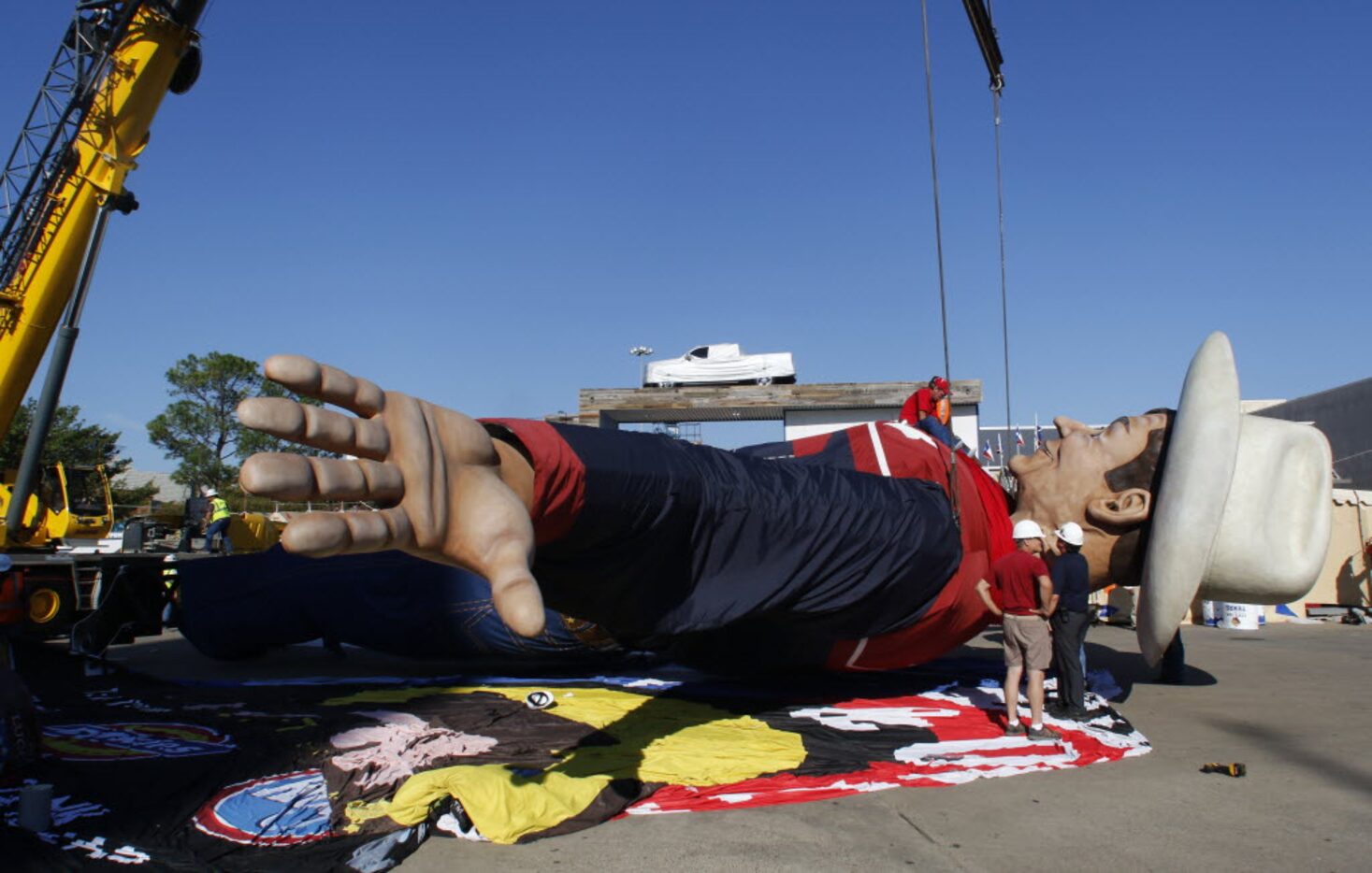 Workers sit on Big Tex’s chest as they adjust his western shirt that runs a size 200 x 325,...