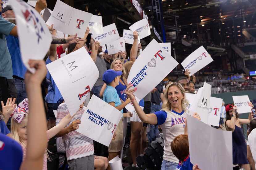 Monument Realty employees hold up signs during a Texas Rangers game where they announced...