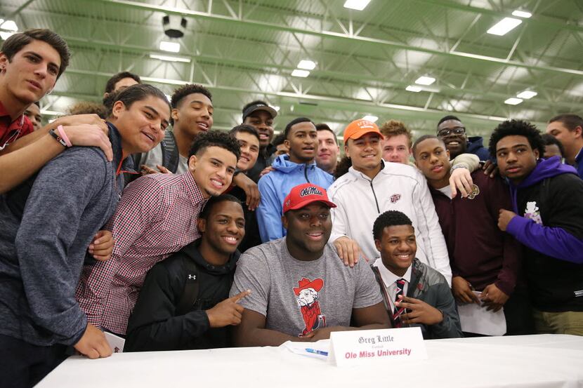 Allen football player Greg Little (center, in gray) is surrounded by teammates after signing...