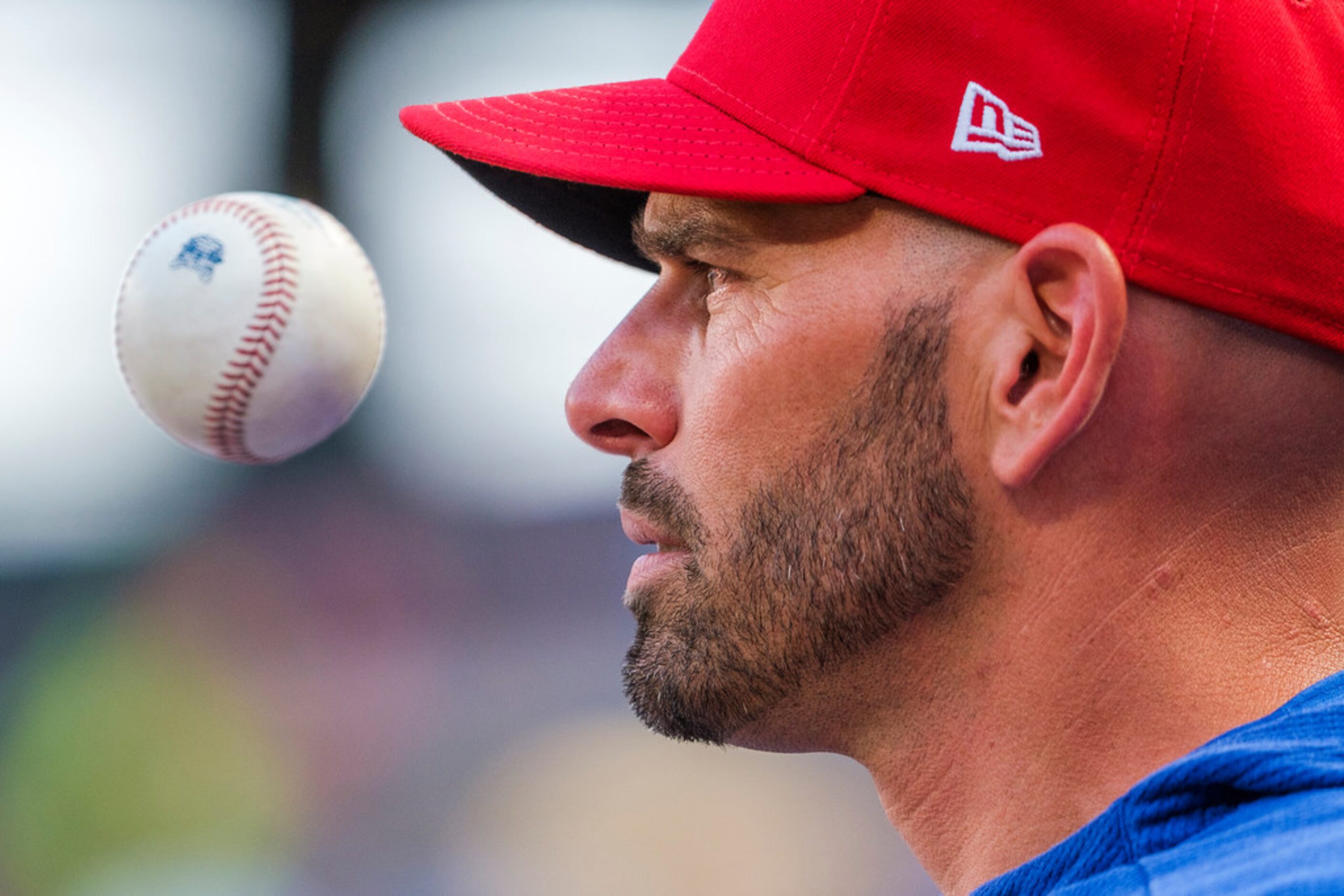 Texas Rangers manager Chris Woodward tosses a ball while watching from the dugout during the...