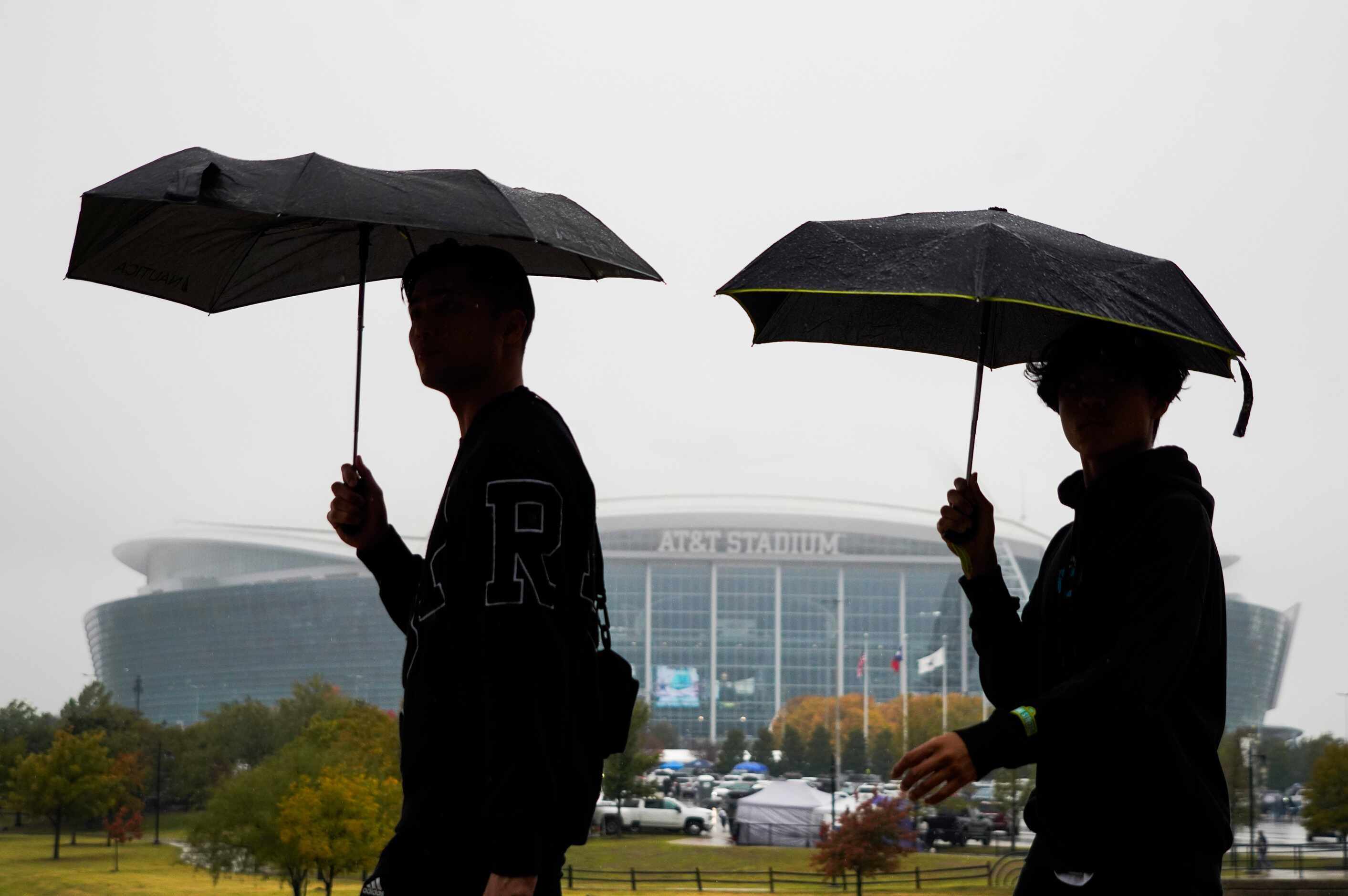 Fans take cover from rain as they head to the stadium before an NFL football game between...