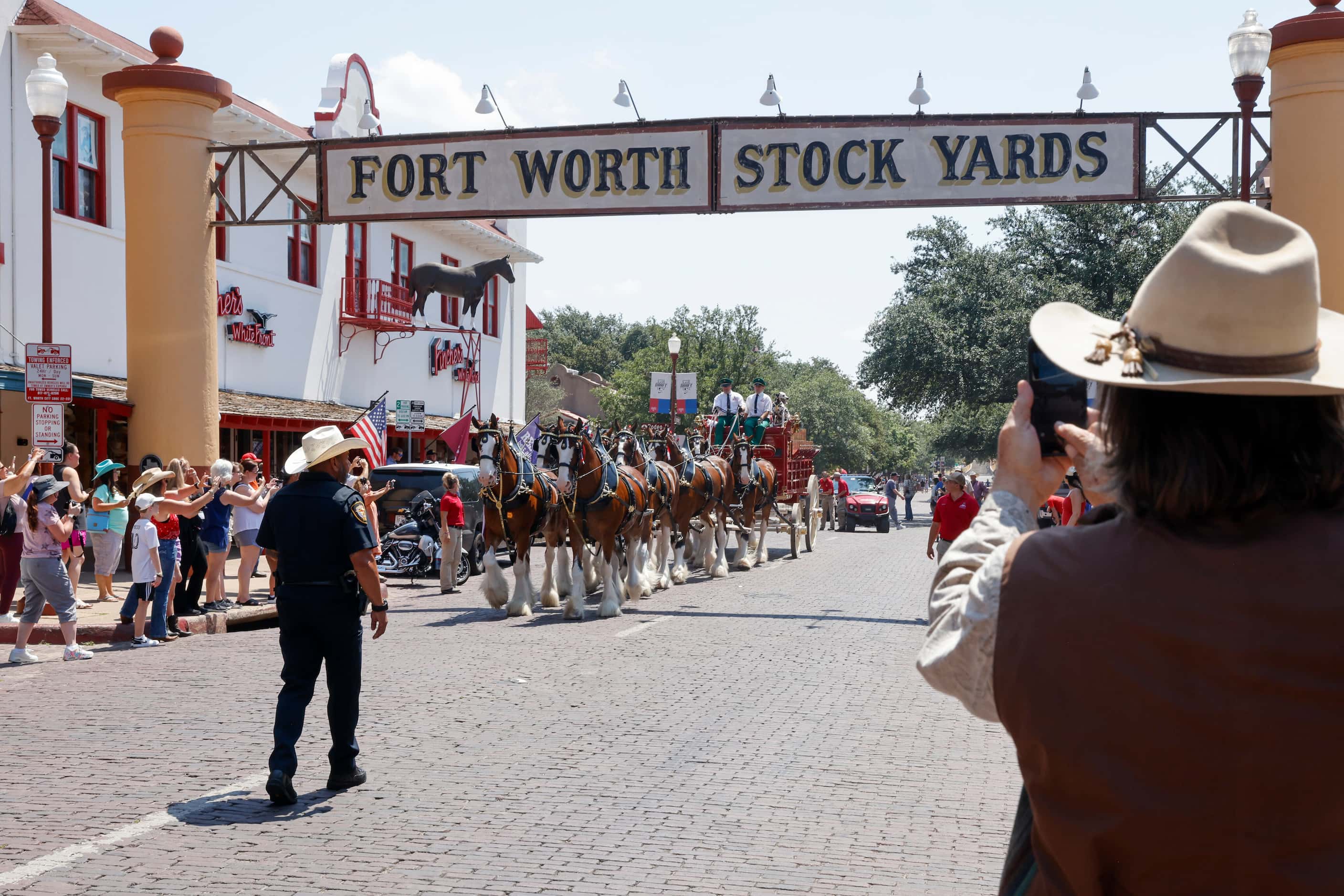 People take photos as the Budweiser Clydesdales pass under the Fort Worth Stockyards sign...
