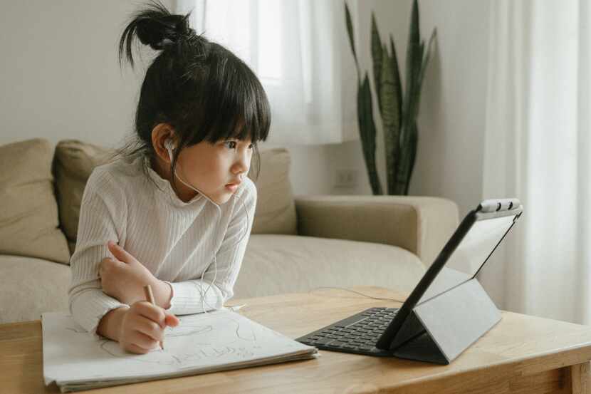 Young Asian girl works participates in virtual learning in front of a laptop in her living...