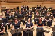 A diverse group of musicians sits onstage with their instruments at Carnegie Hall