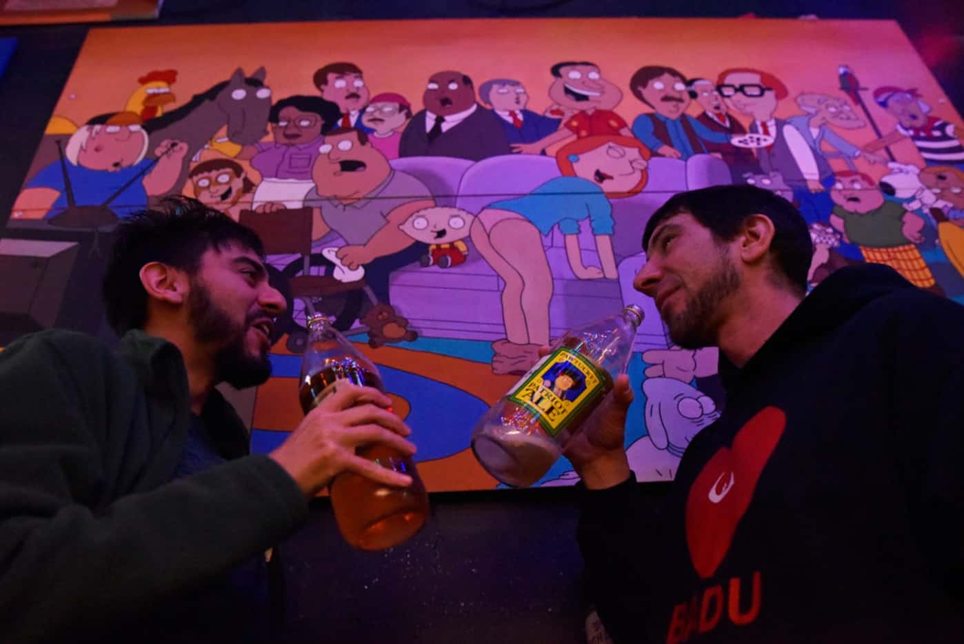 Nick Vasquez, 25, and Bob Warke, 40, drink 40 oz beers near Family Guy art work inside the...