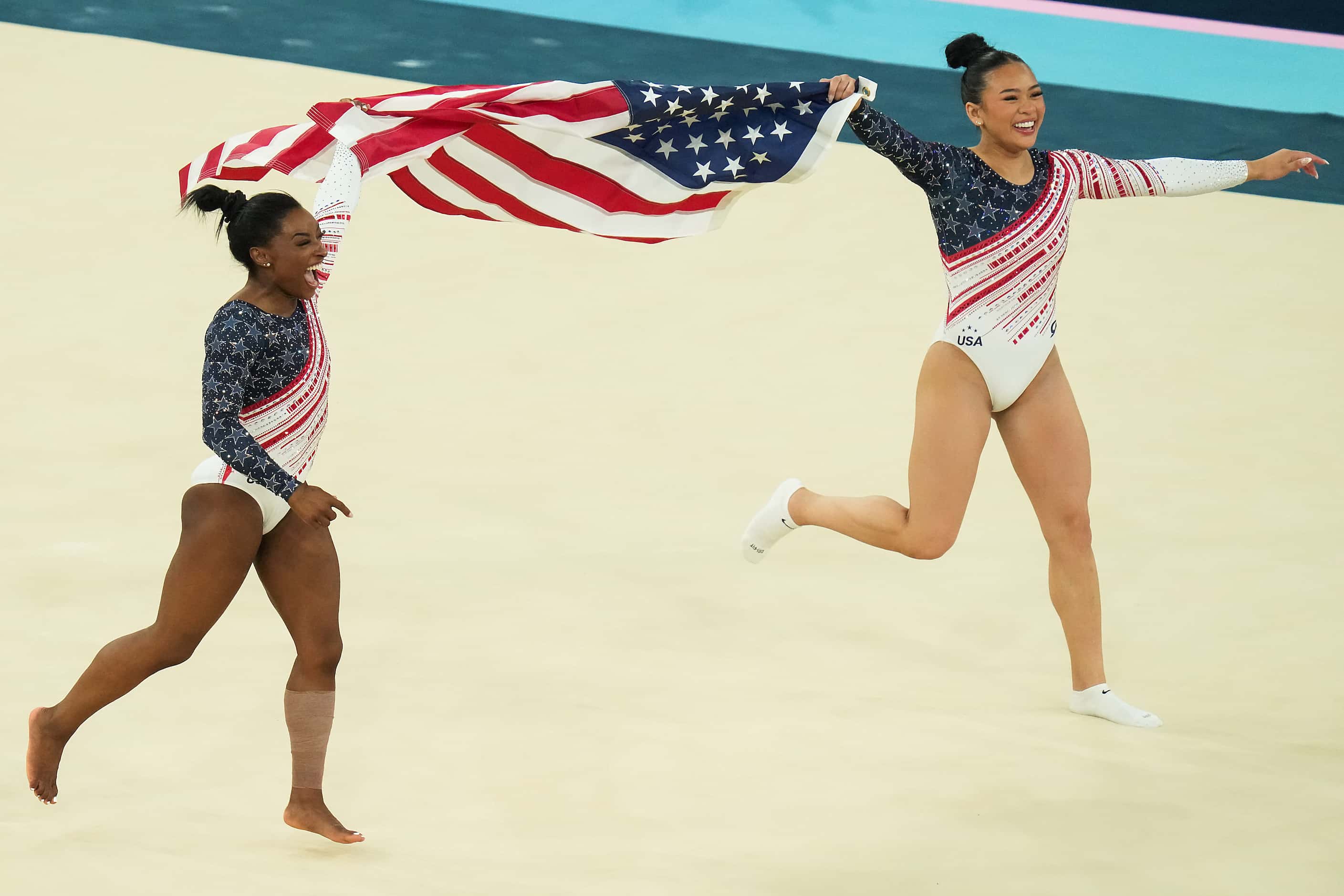 Simone Biles (left) and Suni Lee of the United States carry the flag as they celebrate...