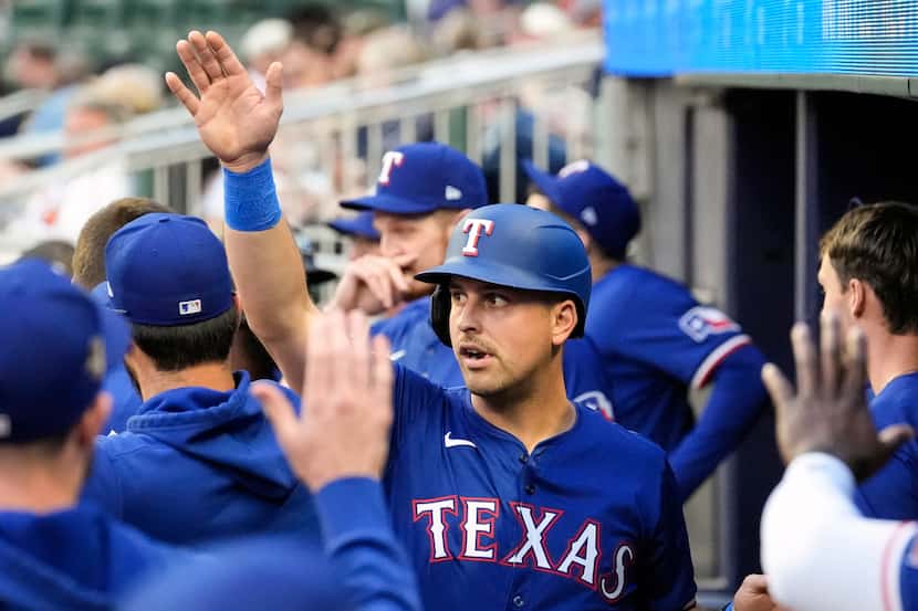 Texas Rangers' Nathaniel Lowe reacts in the dugout after scoring on a Andrew Knizner ground...