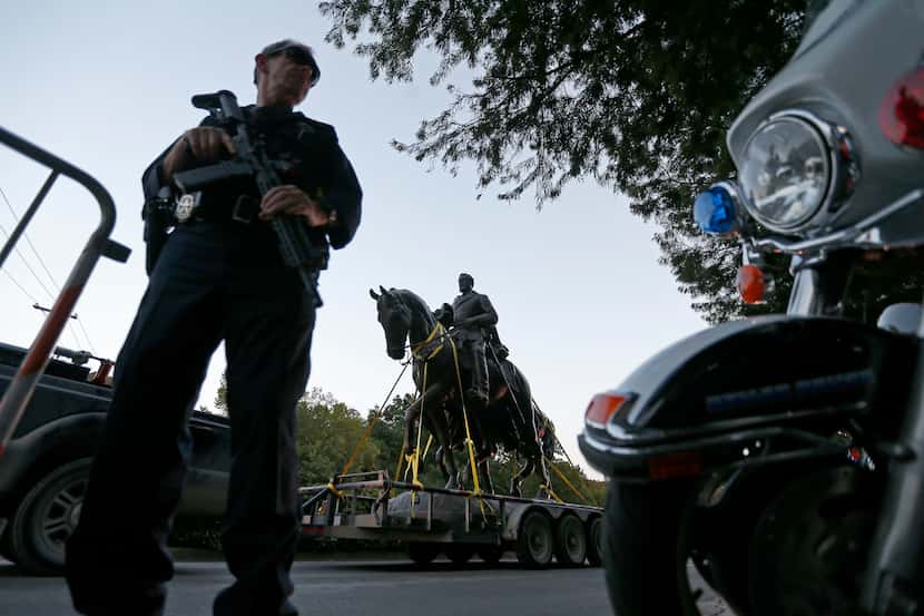 A Dallas Police officer secures an area as a truck carries the Robert E. Lee statue at...