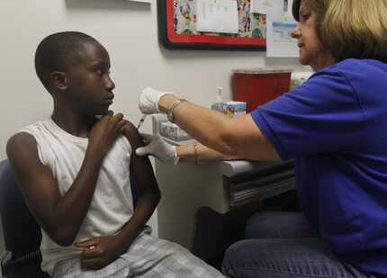 Corey Brooks, 11, gets one of four immunizations from registered  nurse Kathy Collar at the...