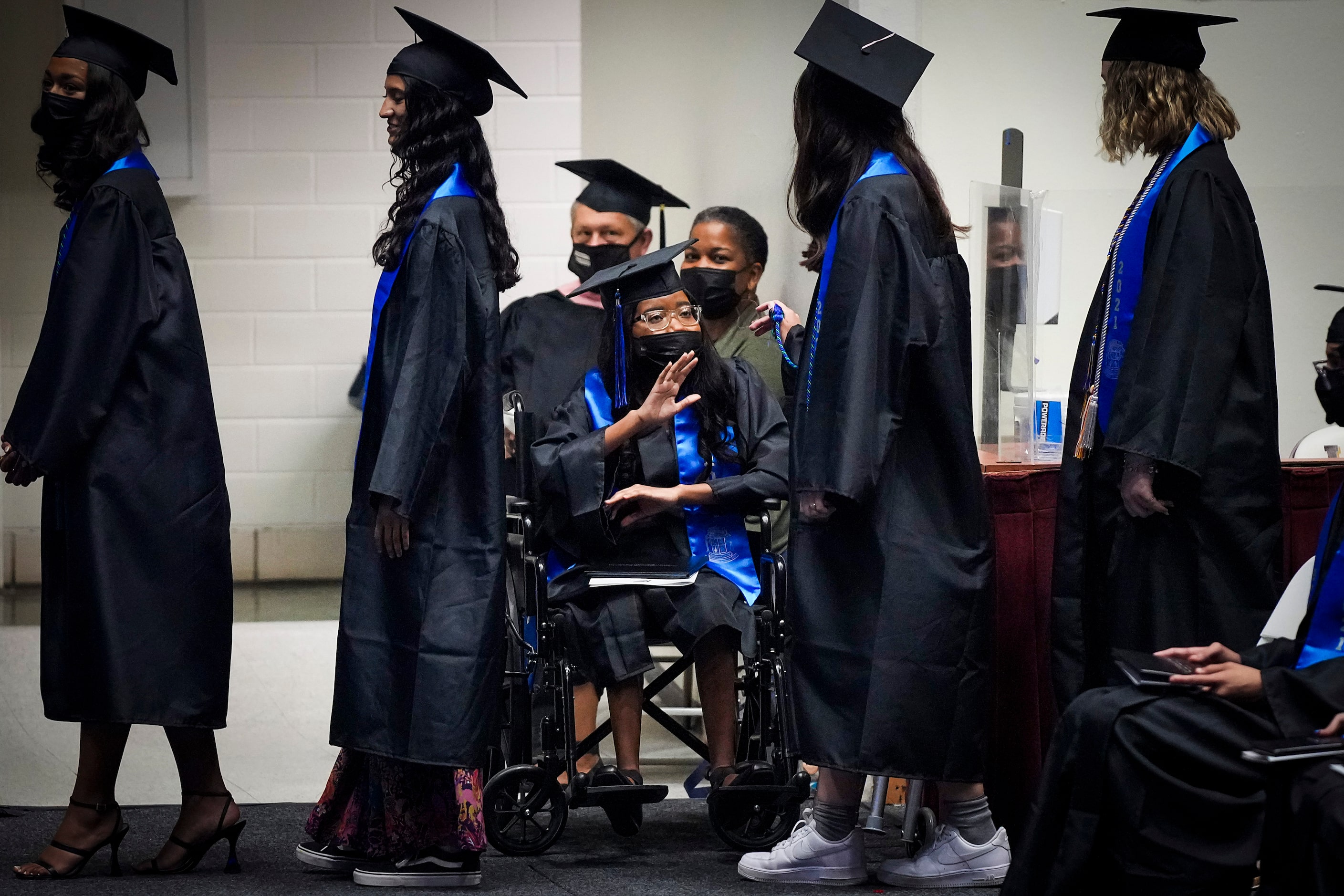 Eryn Fayson waves to classmates from her wheelchair as they process to receive their...