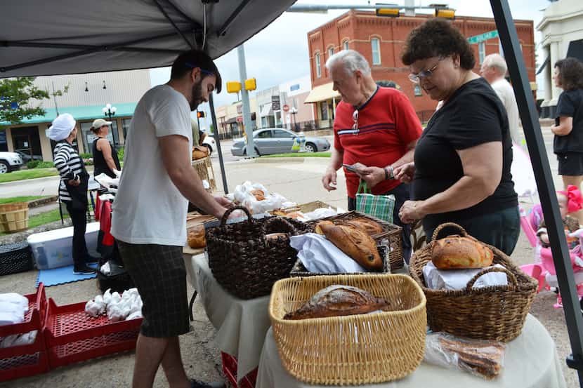 Shaun Cowles (left) sells bread to Steve and Shirlee Ramage at the Village Baking Co. stand...