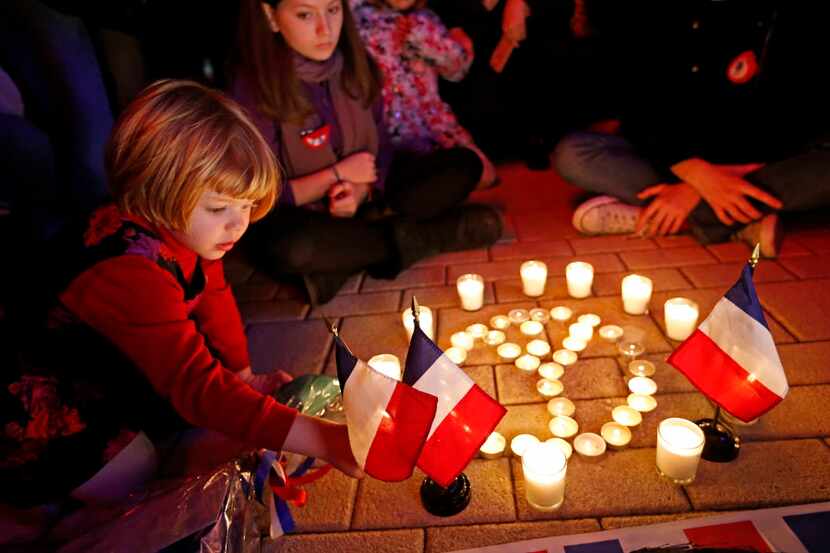  Elizabeth-Anne Browning, 3, of Oak Cliff, places a French flag at a makeshift memorial in...
