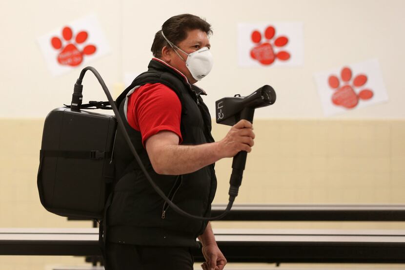 Julian Cruz, a custodian with Garland ISD, sprays a disinfectant in the cafeteria at...