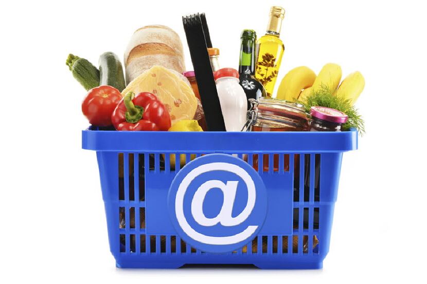 Plastic shopping basket with variety of grocery products isolated on white
