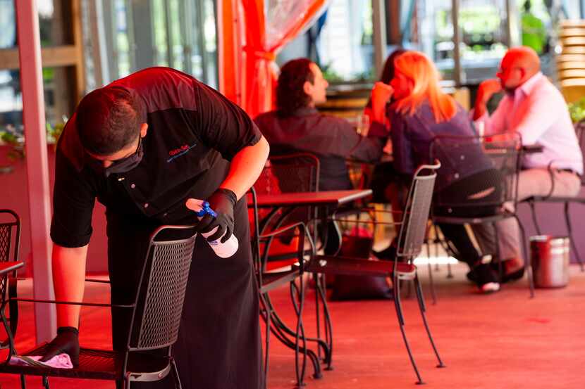 A worker cleans a table on the outside patio of Beto & Son at Trinity Groves on May 1, 2020...