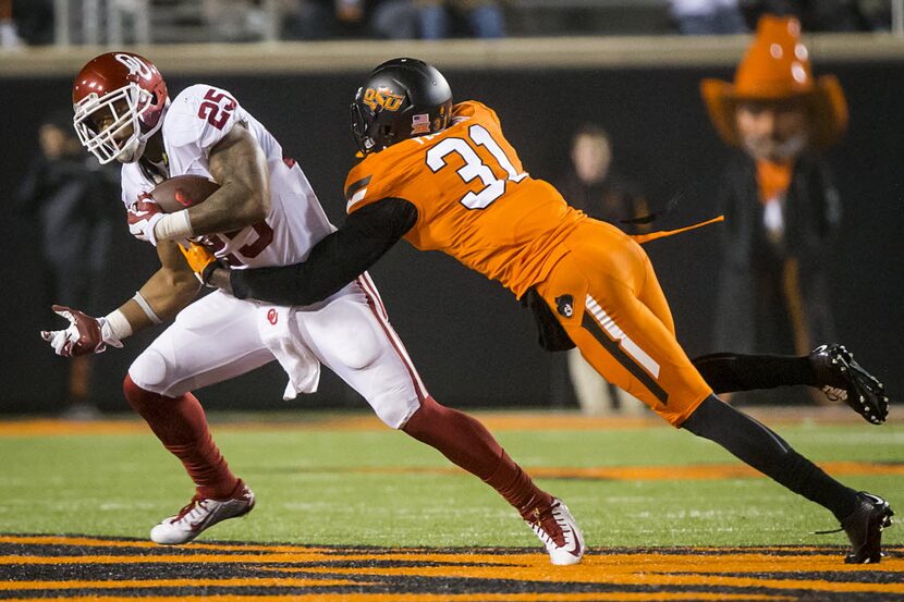 Oklahoma running back Joe Mixon (25) slips past Oklahoma State safety Tre Flowers (31)...