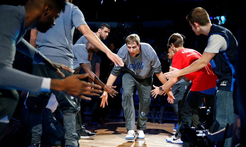 Dallas Mavericks forward Dirk Nowitzki slaps hands with fans and teammates as he is...