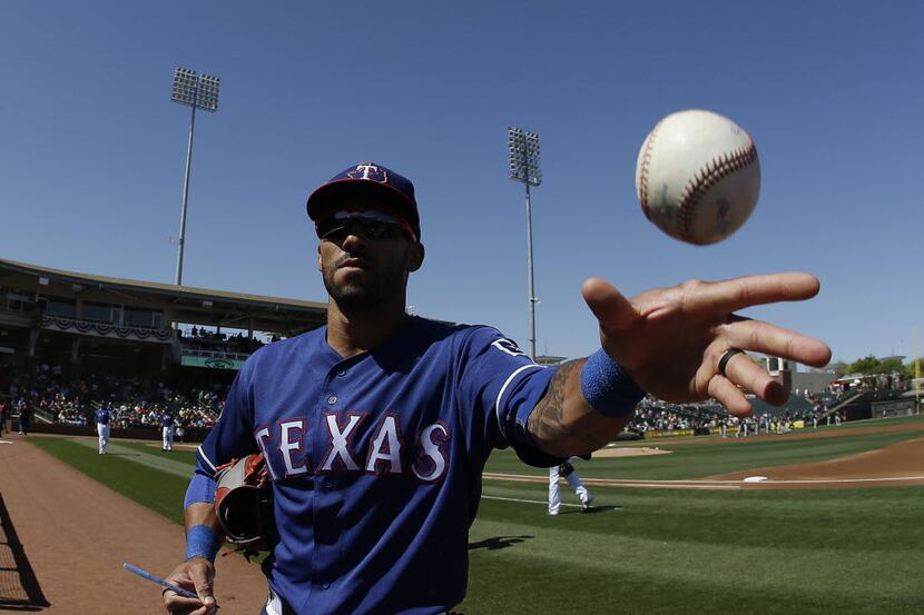 Texas Rangers' Ian Desmond tosses a baseball to a fan before a spring training baseball game...