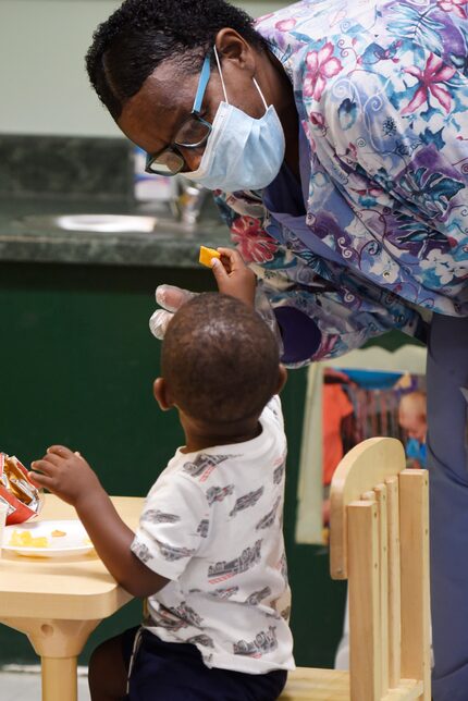 A 2-year-old boy tries to feed Sheila Greer a cracker as she works with him at For Keeps...