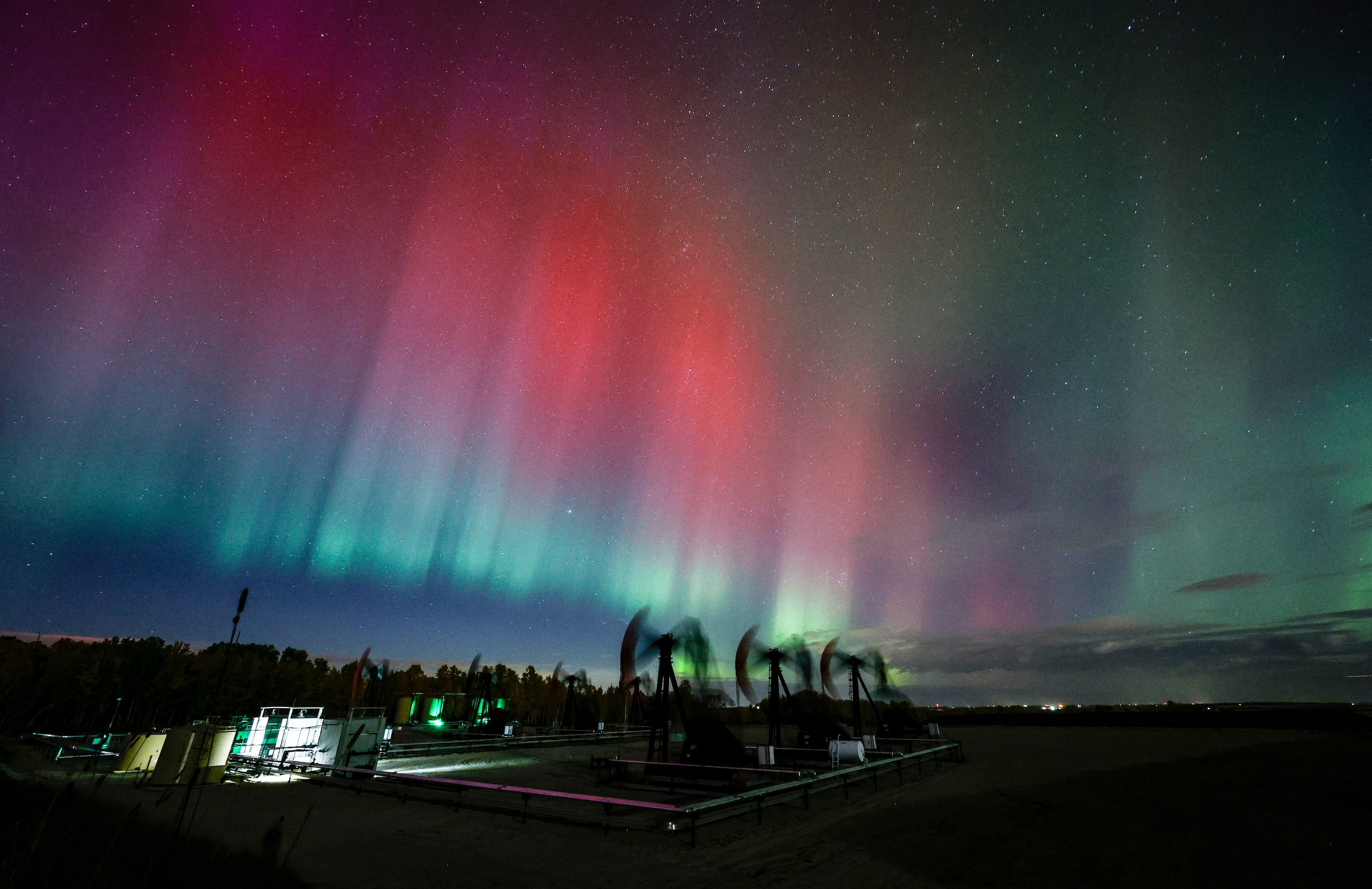 An aurora borealis, also known as the northern lights, makes an appearance over pumpjacks as...