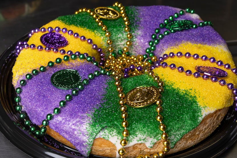 A king cake decorated with Mardi Gras beads and coins pictured at Haute Sweets Patisserie in...