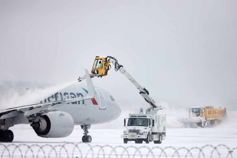 Aerial crews deice an American Airlines jet before it can take off as a plow clears the...