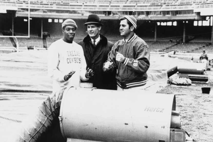 Dallas coach Tom Landry (center) takes a break to warm up at heater in Cleveland Municipal...