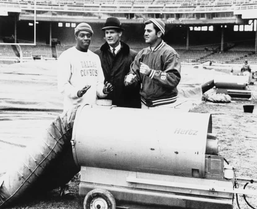 Dallas coach Tom Landry (center) takes a break to warm up at heater in Cleveland Municipal...
