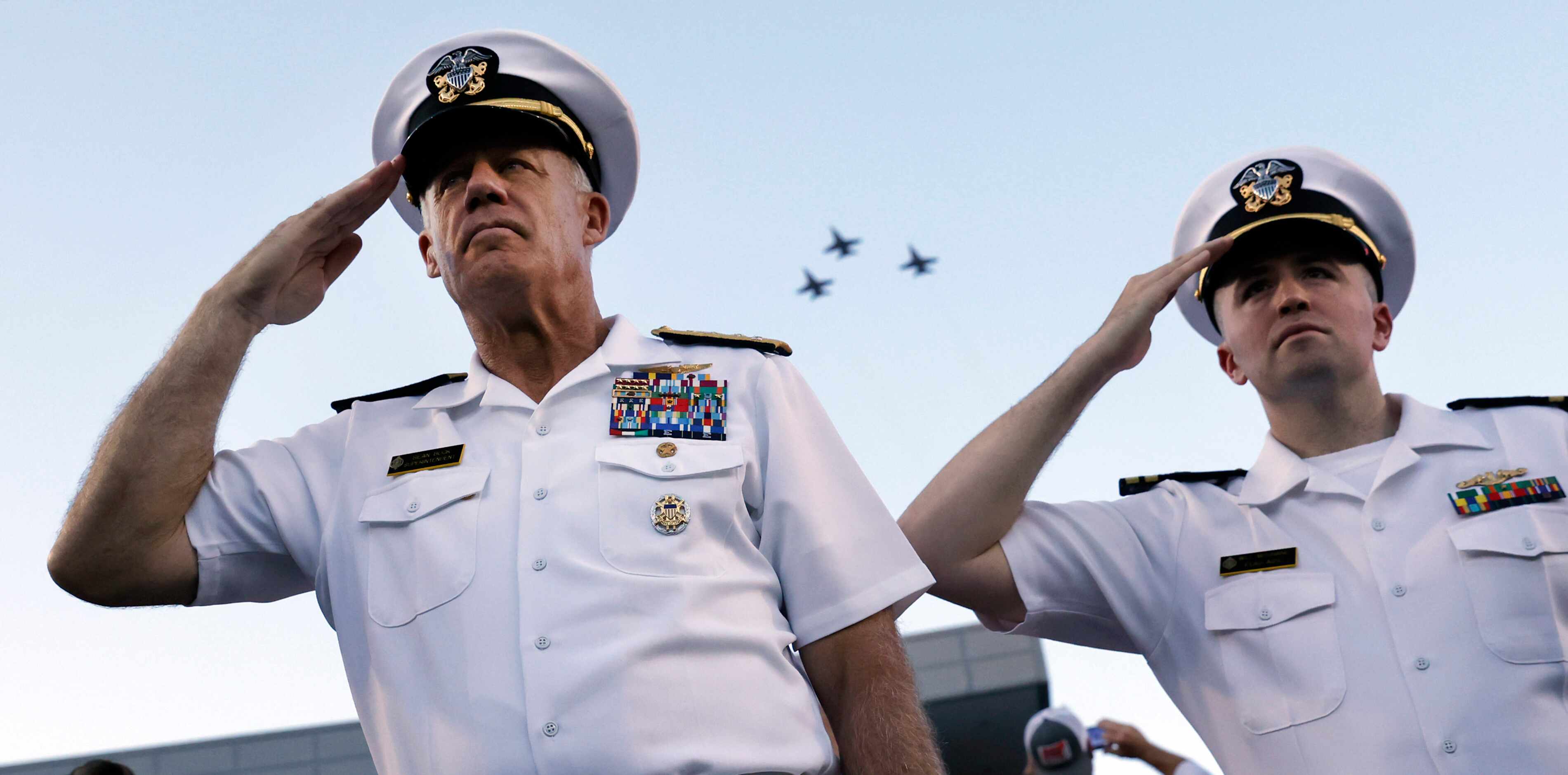 U.S. Navy officers salute as a trio of F-18 military aircraft fly over Gerald Ford Stadium...