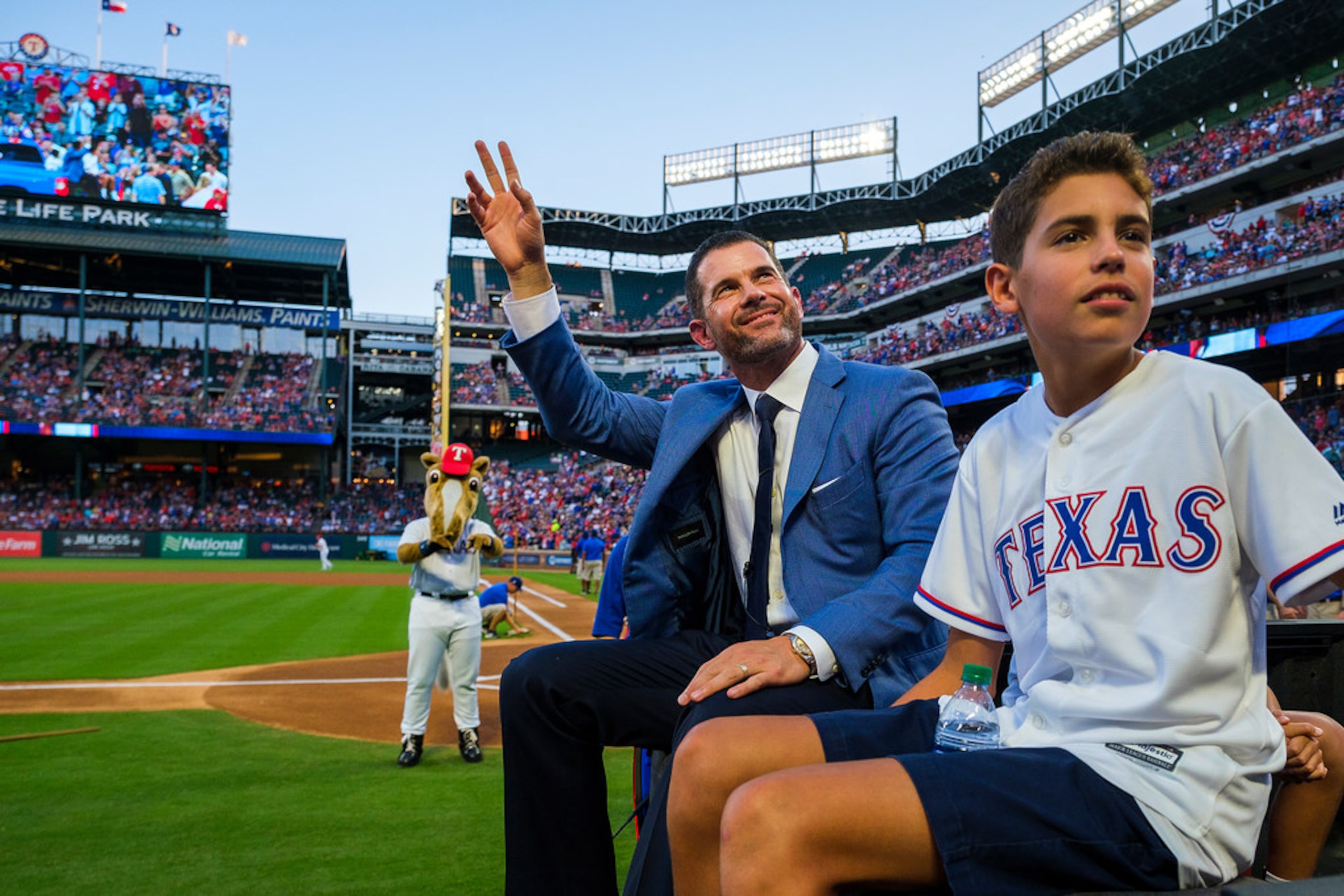 Michael Young waves to the crowd as he rides in a truck with his son Matteo after ceremonies...