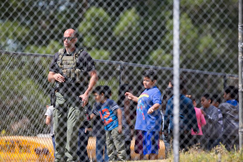 A SWAT officer stands guard with evacuated children on the playground after a shooting...
