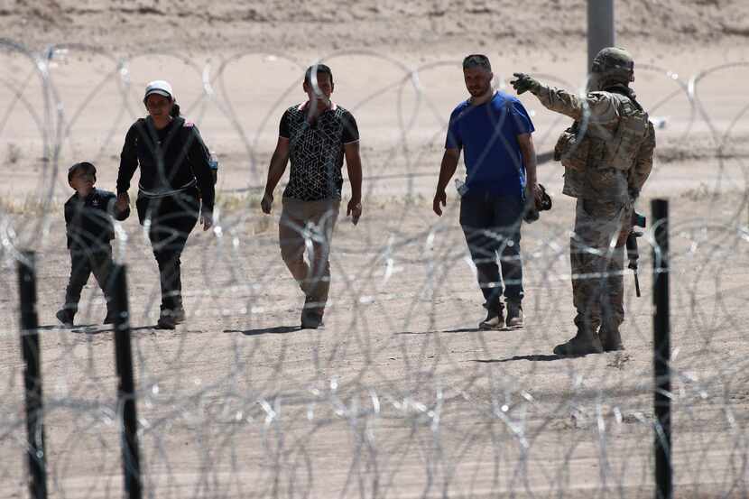 FILE - Migrants wait for U.S. authorities, between a barbed-wire barrier and the border...
