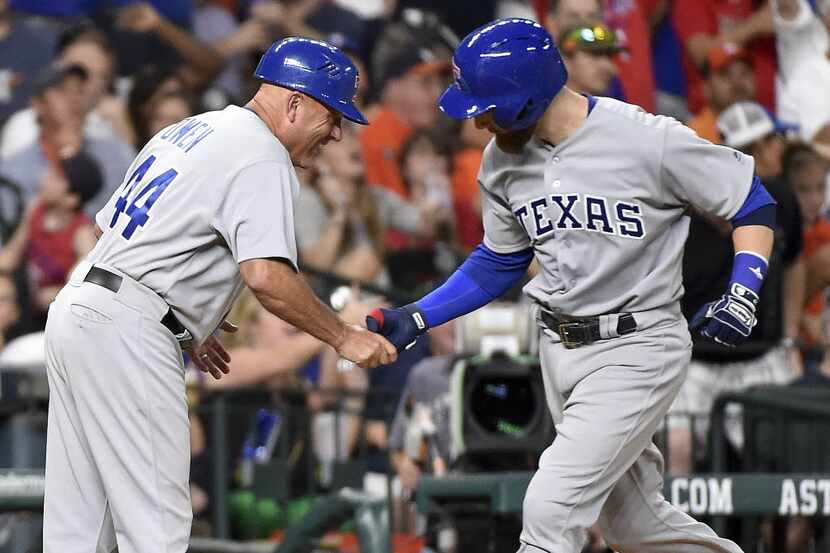 Texas Rangers' Jonathan Lucroy, right, shakes hands with third base coach Spike Owen after...