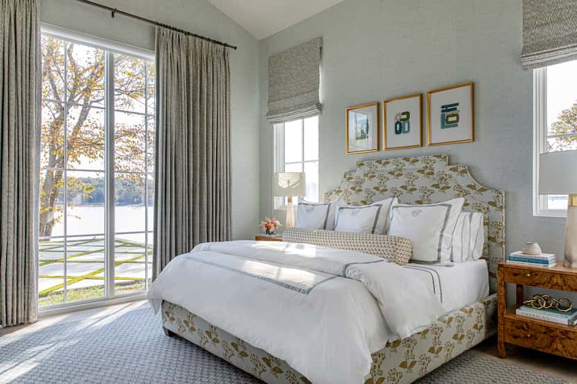 Bedroom with large window looking out to a lake, with a patterned upholstered bed and white...