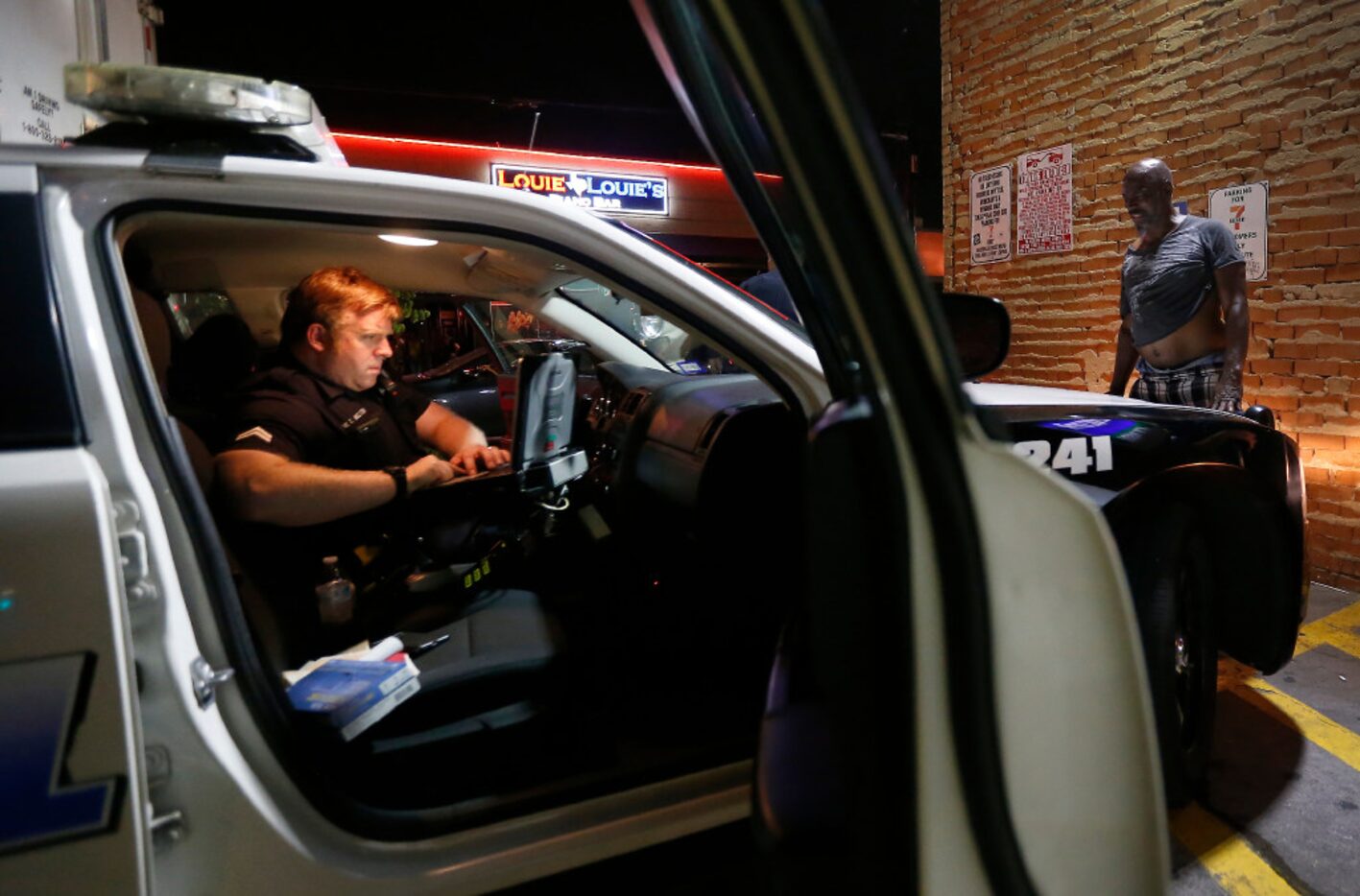 Officers Whitt Melton checks the criminal record of a panhandler in the parking lot of a...