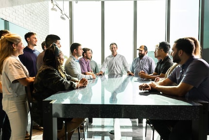 Jason Weeks meets with his team around a table with glass windows behind him at construction...