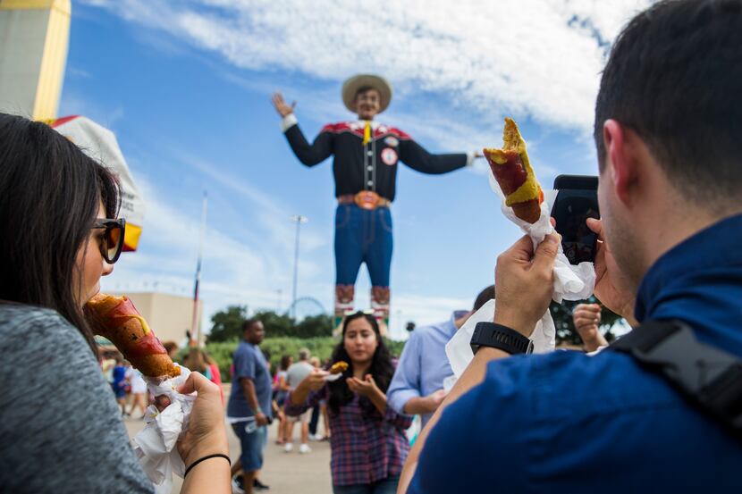 Fairgoers eat Fletcher's Corny Dogs while taking photos of Big Tex on Wednesday, October 4,...