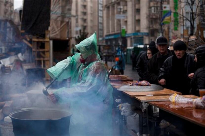 A woman uses a ladle to pour soup into a cup to serve people queuing for free food during a...