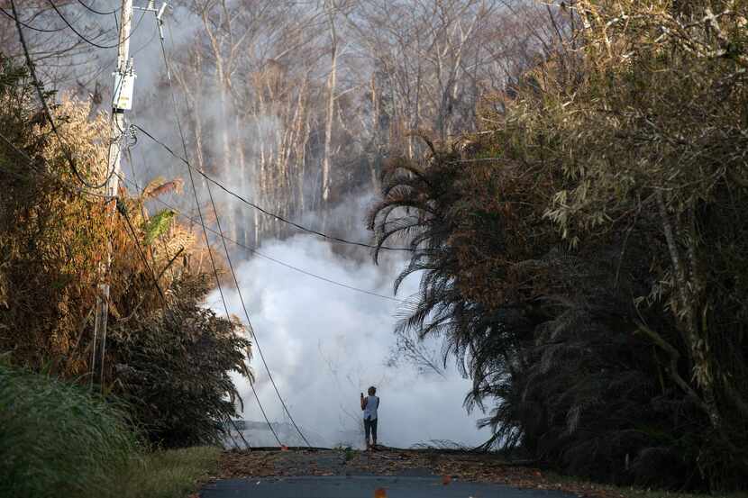 A woman photographs steam and volcanic gas rising from a fissure on Kahukai Street  in the...