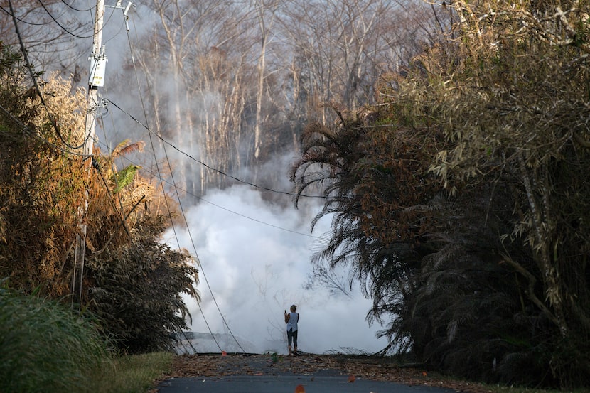 A woman photographs steam and volcanic gas rising from a fissure on Kahukai Street  in the...