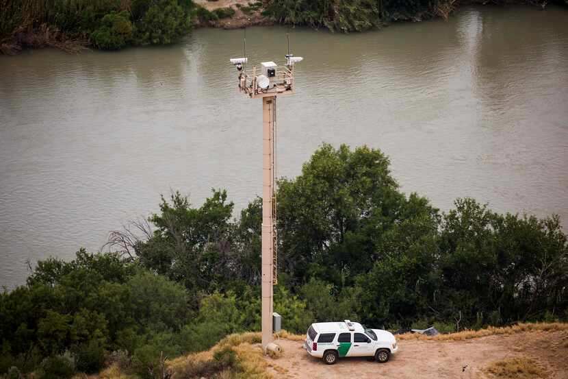 A U.S. Customs and Border Protection officer watches from a vehicle at the base of a camera...