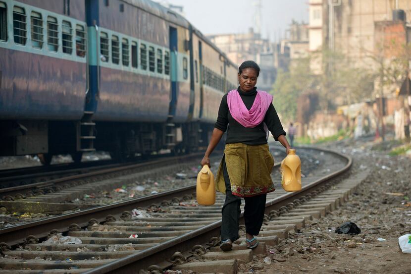 An Indian woman who lives near the railway tracks fetches drinking water in plastic...