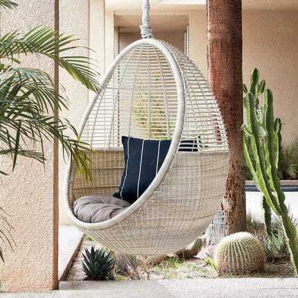 A white hanging chair with cactus in the background.